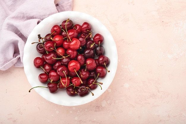 Fresh sweet cherry in white heart-shaped plate for Valentines Day on gray background. Concept for a romantic treat or meal. Top view. Mock up.