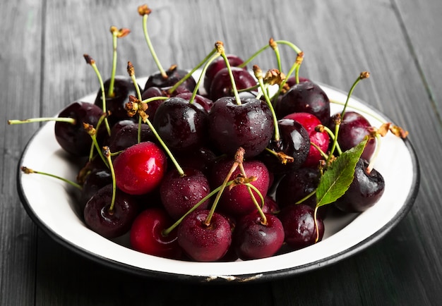 Fresh sweet cherry in a white plate on a dark wooden background.