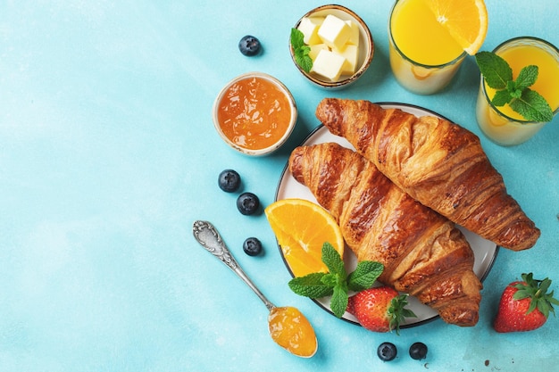 Fresh sweet croissants with butter and orange jam for breakfast Continental breakfast on a bright concrete table Top view with copy space Flat lay