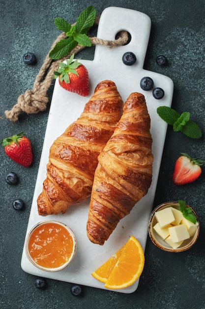 Fresh sweet croissants with butter and orange jam for breakfast Continental breakfast on a dark concrete background Top view Flat lay