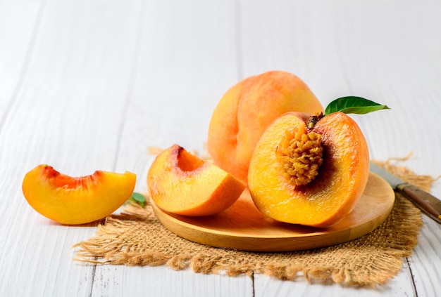 Fresh sweet sliced peach with green leaf on wood plate. Peach fruits