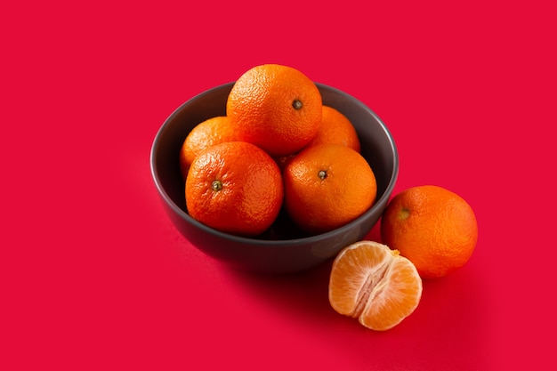 Fresh tangerines in bowl on red table