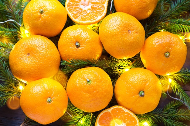 Fresh tangerines in garland lights, on fir branches and tinsel - new year's bright background. Half of an orange, citrus aroma of the holiday. Christmas, New year. Space for text.