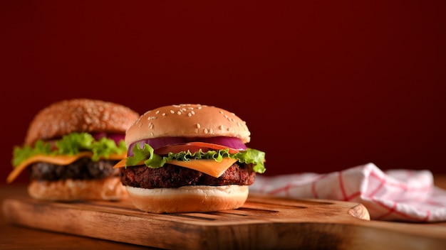 Fresh tasty beef burgers served on wooden tray on the table with napkin in restaurant with red wall