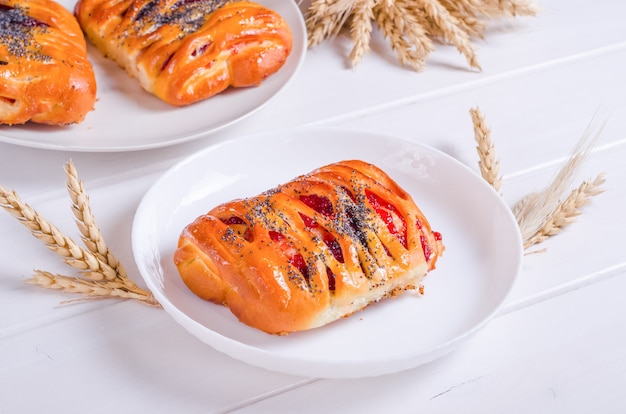 Fresh tasty bun with berry filling on white plate on white wooden background