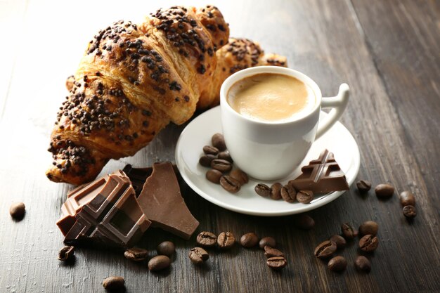 Fresh and tasty croissants with chocolate and cup of coffee on wooden background