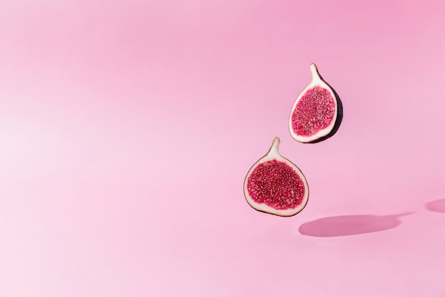 Fresh tasty fig fruit halves levitation with shadow on pink background. Two cross sections of fig falling down or fly. Vegan desert concept. Shadow of flying healthy eating food. High quality photo