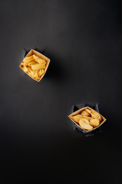 Fresh tasty french fries sticks out through torn holes in paper background street food concept