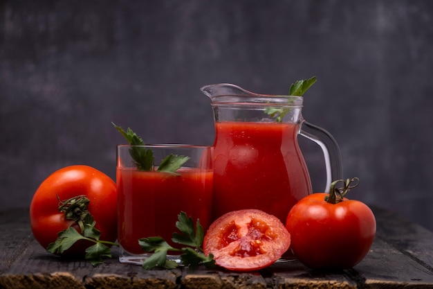 Fresh tomato juice in a glass with tomatoes with parsley on a dark background