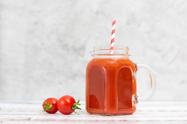 Fresh tomato juice in jar and cherry tomatoes on light background