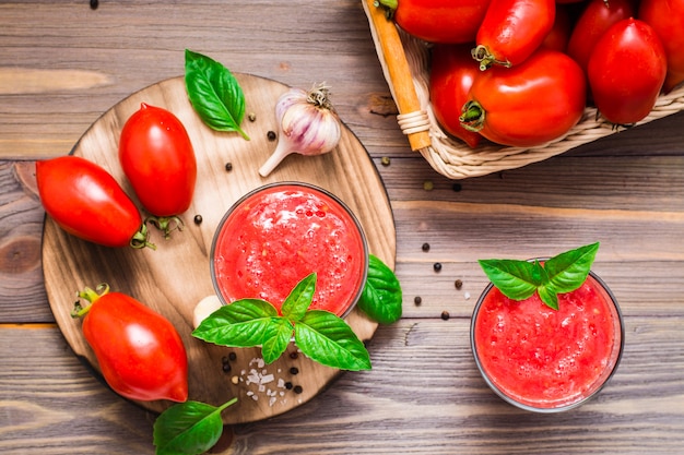 Fresh tomato juice with basil leaves in glasses and ingredients for its preparation on a wooden table. Top view