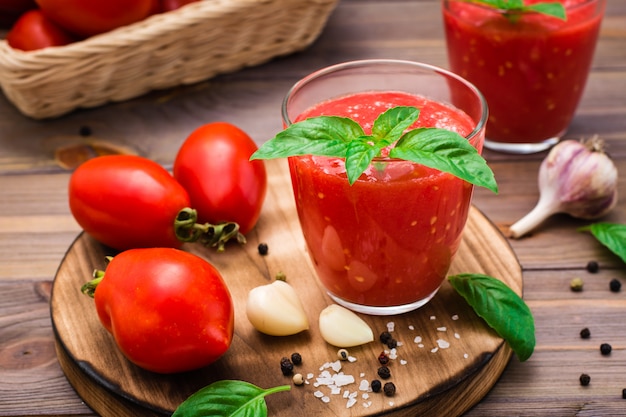 Fresh tomato juice with basil leaves in glasses and tomatoes on a wooden table