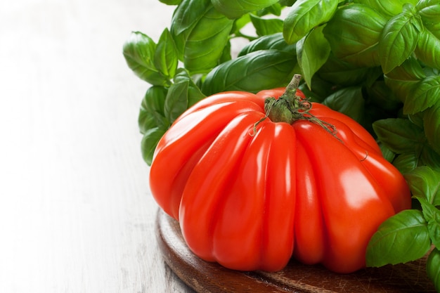 Fresh tomato with basil on old wooden board.