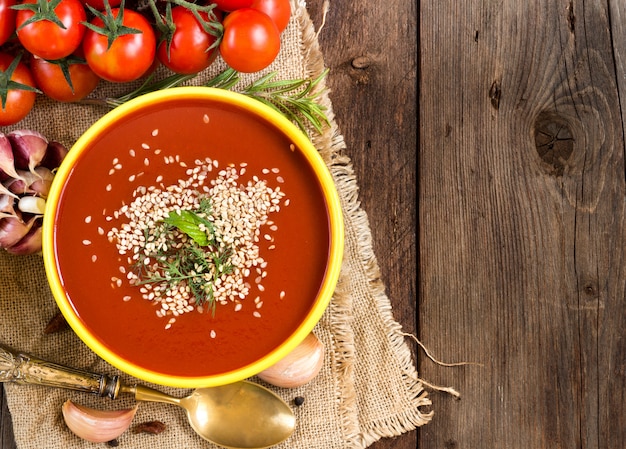 Fresh tomatoe soup puree and raw vegetables on a wooden table with copy space