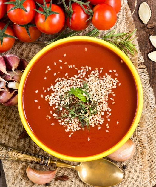 Fresh tomatoe soup puree and raw vegetables on a wooden table with copy space