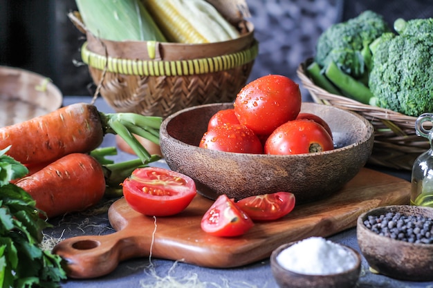 fresh tomatoes in a bowl, around vegetables, carrot, black pepper, corn, broccoli. Slice tomatoes. Harvesting tomatoes. 