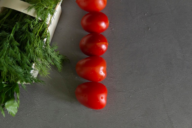 Fresh tomatoes and dill greens with parsley in a basket of vines lie on a gray table