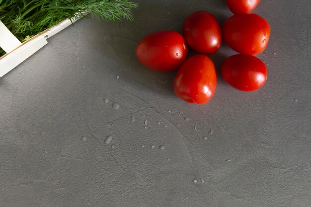 Fresh tomatoes and dill greens with parsley in a basket of vines lie on a gray table