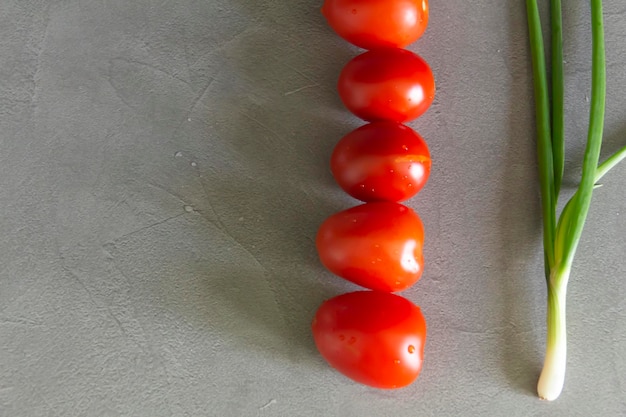 Fresh tomatoes and green onions plucked from the garden are on the gray working surface of the kitchen