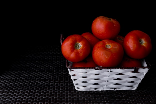 Fresh tomatoes on a plate on a dark background. a basket full of tomatoes