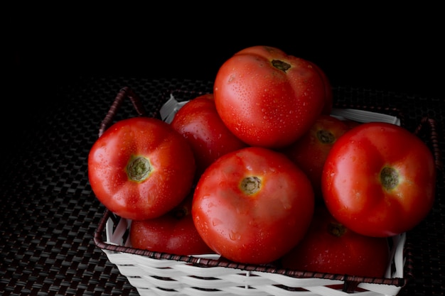 Fresh tomatoes on a plate on a dark background. a basket full of tomatoes