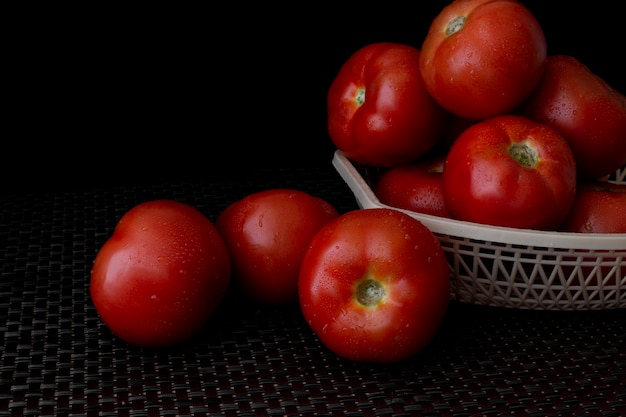 Fresh tomatoes on a plate on a dark background. a basket full of tomatoes