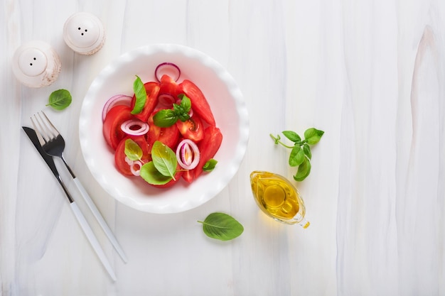 Fresh tomatoes salad with basil leaves olive oil and onion in white bowl on light background Traditional italian or mediterranean food diet Top view