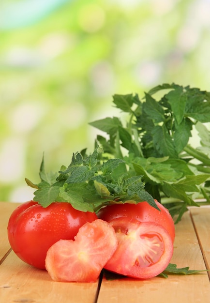 Fresh tomatoes and young plant on wooden table on natural background