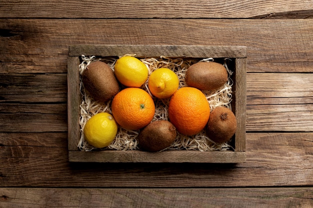 Fresh tropical fruits in a wooden delivery box on a wooden background. Orange, kiwi and lemon top view flat lay with copy space for some advertisement text