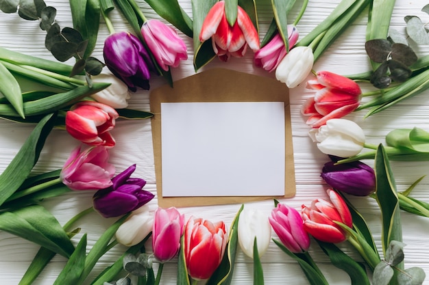 Fresh tulips around a postcard with copy space. Mothers day concept, top view.