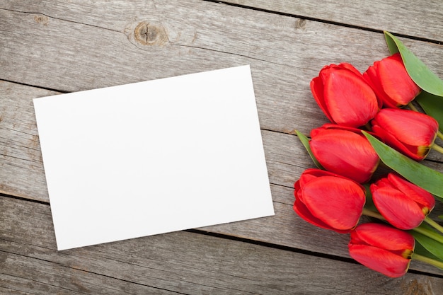 Fresh tulips and greeting card over wooden table background