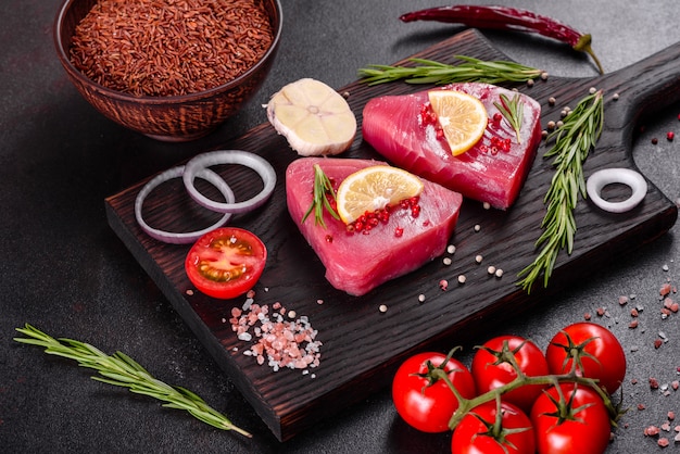 Fresh tuna fillet steaks with spices and herbs on a black background