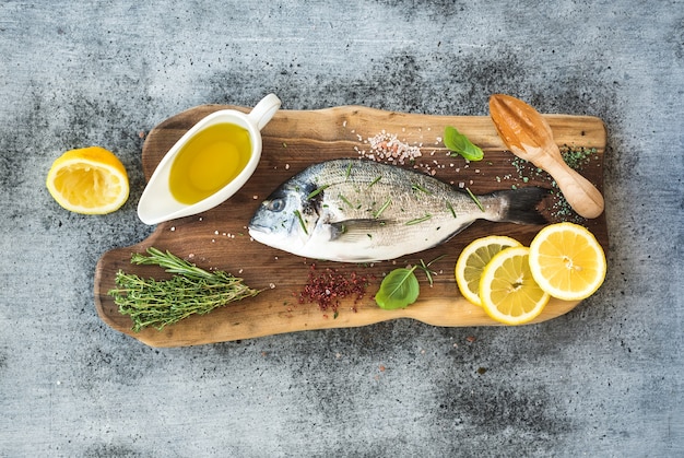 Fresh uncooked dorado or sea bream fish with lemon, herbs, oil and spices