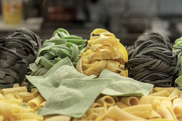 Fresh uncooked pasta and homemade ravioli with spinach and cuttlefish ink are rolled up on the table.