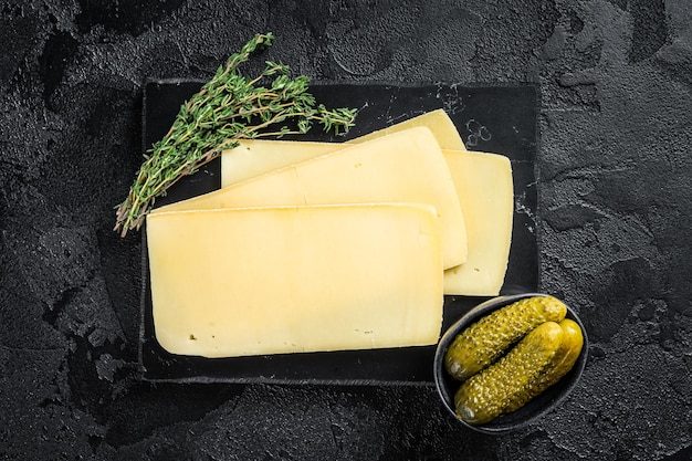 Fresh Uncooked Raclette Swiss cheese slices on marble board Black background Top view