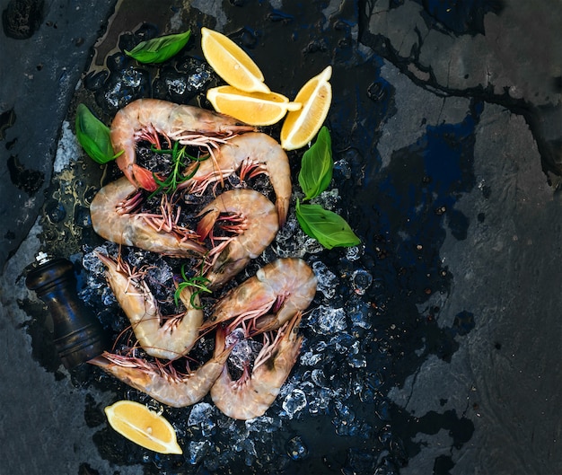 Fresh uncooked shrimps with lemon, herbs and spices on chipped ice