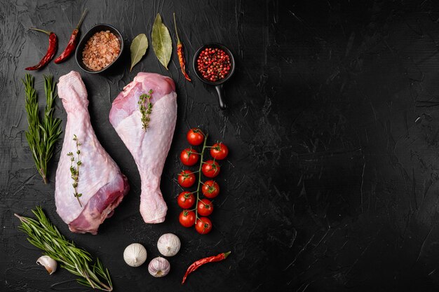 Fresh uncooked turkey legs set, on black dark stone table background, top view flat lay, with copy space for text