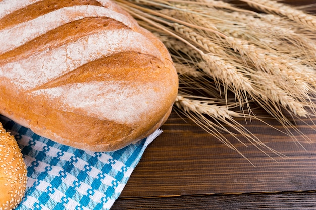 Fresh uncut large crusty French baguette with ears of golden ripe wheat on a wooden table, close up view