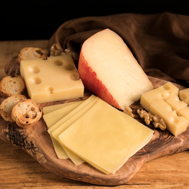 Fresh variety of cheeses with walnut and bread on wooden textured tray