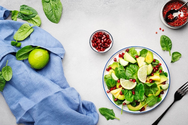 Fresh vegan salad with pineapple spinach avocado and pomegranate seeds gray kitchen table top view Healthy eating clean food diet weight loss concept