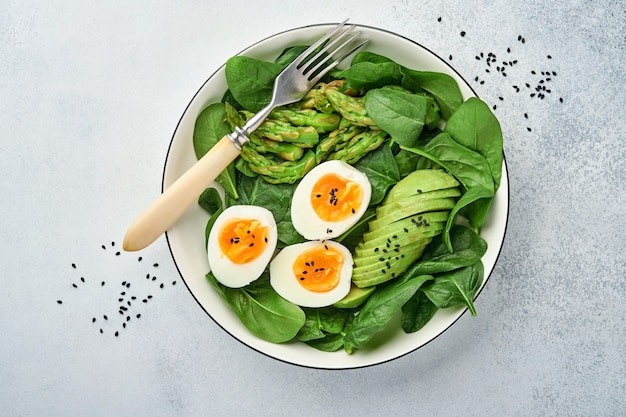 Fresh vegetable salad with avocado, asparagus, boiled eggs on light concrete surface. Top view.