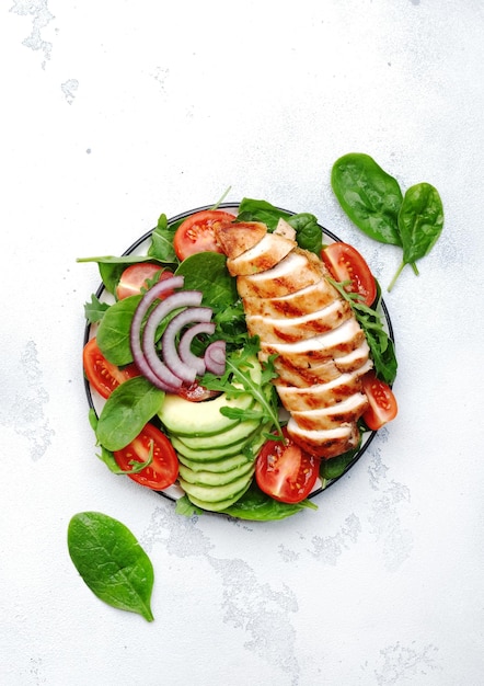 Fresh vegetable salad with grilled chicken fillet spinach tomatoes avocado and red onion with olive oil on white background Healthy detox ketogenic diet food Top view