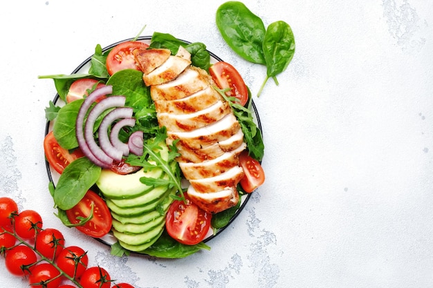 Fresh vegetable salad with grilled chicken fillet spinach tomatoes avocado and red onion with olive oil on white background Healthy detox ketogenic diet food Top view