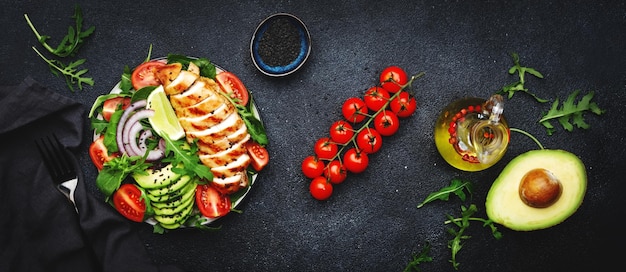 Fresh vegetable salad with grilled chicken fillet spinach tomatoes avocado sesame seed and red onion on black background Healthy detox ketogenic diet food Top view banner