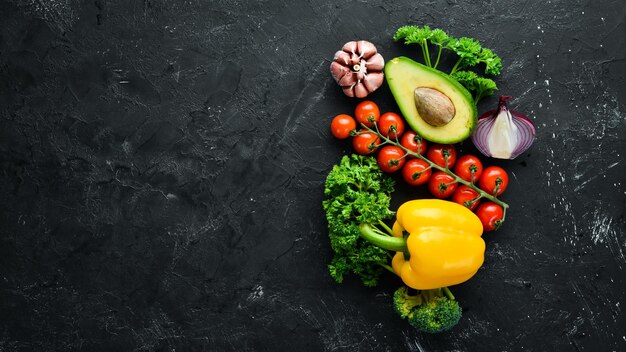 Fresh vegetables on a black background Avocados tomatoes garlic parsley paprika Top view Free space for your text