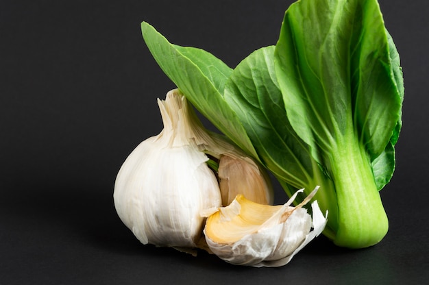 Fresh vegetables: bok choy or chinese cabbage and garlic on black background. Healthy food.