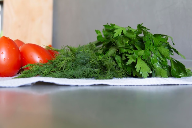 Fresh vegetables cucumbers tomatoes and greens with dill and parsley lie on the kitchen gray surface on a linen towel