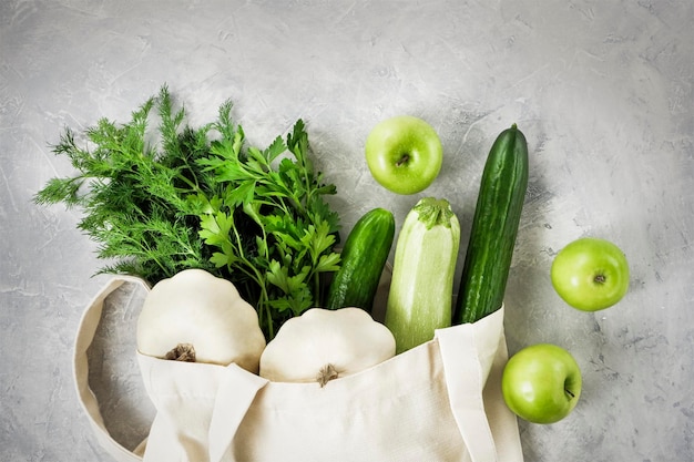 Fresh vegetables fruits greenery in a reusable shopping cotton bag on a concrete gray tabletopfood