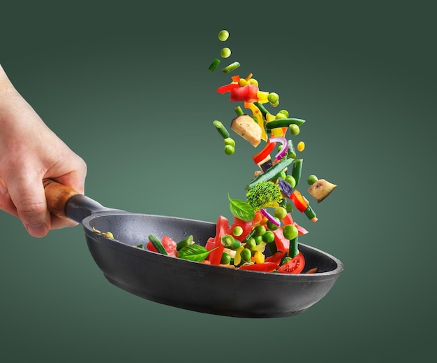 Fresh vegetables in a pan in chef hand on green background