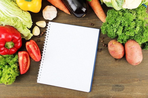 Fresh vegetables and spices and paper for notes on wooden background